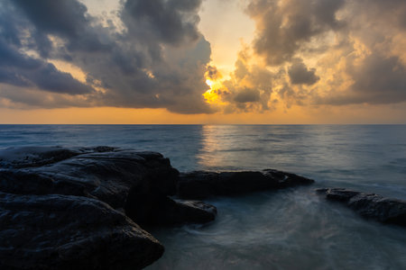 sunrise dramatic sky over sea horizon from rocky shore at dawn long exposure shotの写真素材