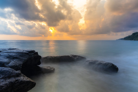 sunrise dramatic sky over sea horizon from rocky shore at dawn long exposure shotの写真素材