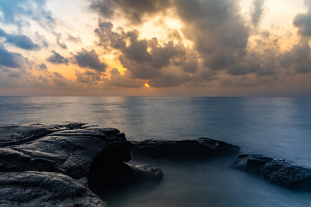 sunrise dramatic sky over sea horizon from rocky shore at dawn long exposure shotの写真素材