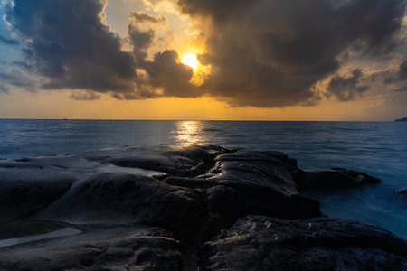 sunset dramatic sky over sea horizon from rocky shore at dawn long exposure shotの写真素材