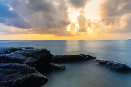 sunrise dramatic sky over sea horizon from rocky shore at dawn long exposure shotの写真素材