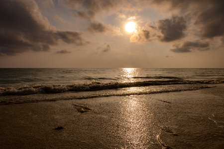 sea horizon with bright sunset orange sky from sandy beach and rolling waves at morningの写真素材