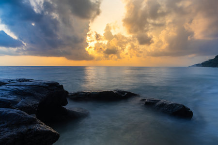 sunrise dramatic sky over sea horizon from rocky shore at dawn long exposure shotの写真素材
