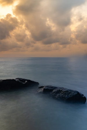 sunrise dramatic sky over sea horizon from rocky shore at dawn long exposure shotの写真素材