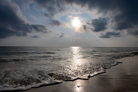 sea horizon with bright sunrise blue sky from sandy beach and rolling waves at morningの写真素材