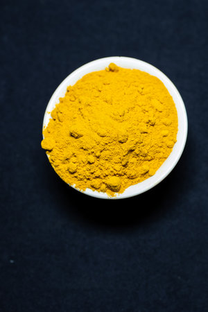 Fresh turmeric powder in ceramic bowl with black Background studio shotの写真素材