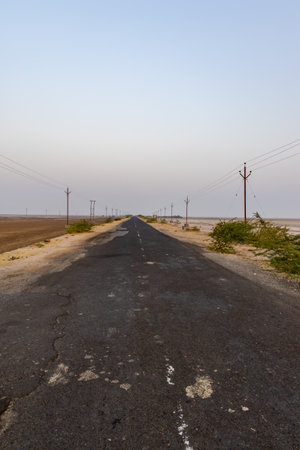 isolated empty tarmac road with electric pole leading to horizon and bright sunrise sky at morningの写真素材