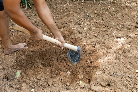 farmer using hand tool to plough soil at farm fieldの写真素材
