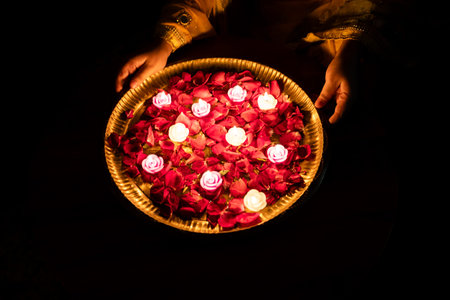 women holding holy plate filled with glowing candles and rose petals on diwali celebration
