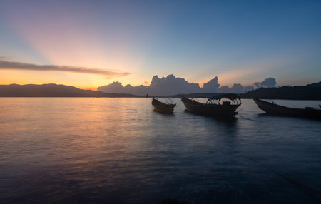 fishing boats anchored in sea backwater under golden sunset skyの写真素材