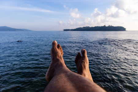 man's bare feet enjoying the view of calm blue ocean and horizonの写真素材