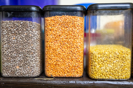 assorted indian lentils and pulses stored in transparent plastic containers on shelf