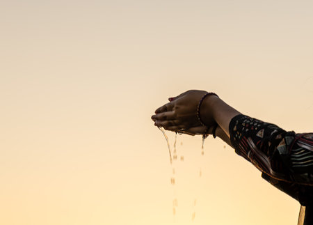 sacred water offering captured as droplets fall from cupped handsの写真素材