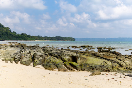 rocky tropical beach with moss covered stones and shallow seaの写真素材