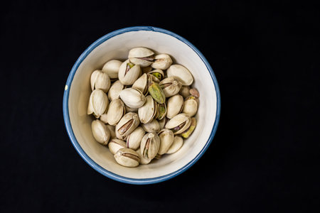 roasted pistachio nuts in ceramic bowl isolated on black background showcasing healthy snack concept