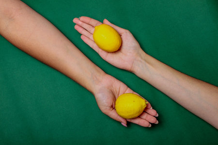Two hands carrying lemons on the green backgroundの写真素材