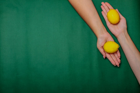 Two hands carrying lemons on the green backgroundの写真素材