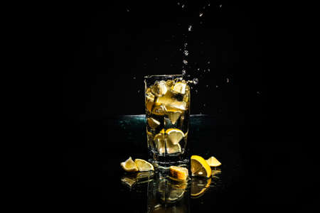 A slice of lemon falls into a glass, black background. Flying water dropsの写真素材