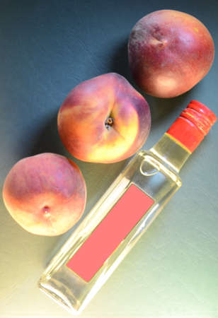 three ripe peaches close-up over a bottle with a pink label on an embossed leathery azure green background, top viewの写真素材