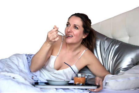 woman sitting in bed eating breakfastの写真素材