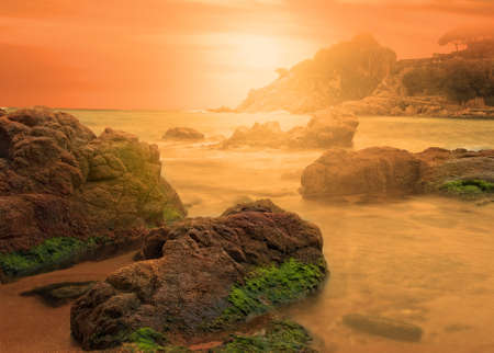 sunrise on the beach with rocks and calm seaの写真素材