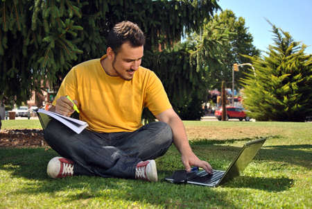college student lying on the grass in the sun with a computerの写真素材
