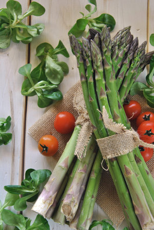 organic asparagus on wooden table accompanied by cherry tomatoes and lettuceの写真素材