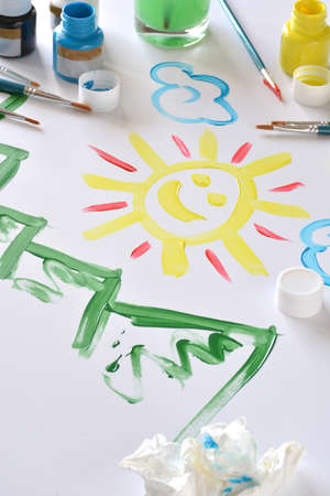 watercolors and brushes with children's drawings on white canvasの写真素材