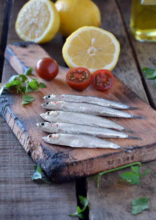 fresh anchovies, placed on a wooden table and accompanied by oil, tomatoes and parsley