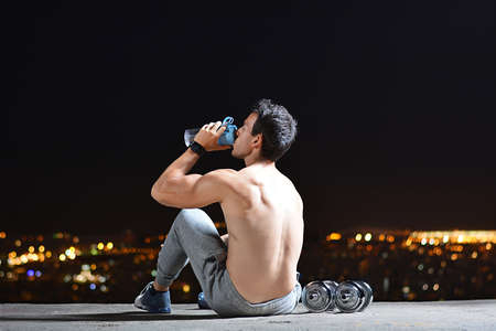 young man training with dumbbells on top of a viewpoint of a cityの写真素材