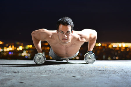 young man training with dumbbells on top of a viewpoint of a city
