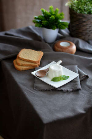 fresh cheese with basil leaves on a white plate and a table with grey cloth. Very healthy and full of protein foodの写真素材