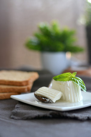 fresh cheese with basil leaves on a white plate and a table with grey cloth. Very healthy and full...