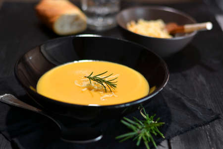 Vegetable soup in black plate and table of dark wood, accompanied by grated cheese and Rosemaryの写真素材