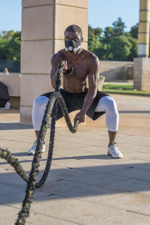 male muscular training with battle ropes and training mask in a park outdoor