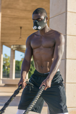 male muscular training with battle ropes and training mask in a park outdoorの写真素材