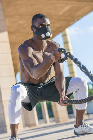 male muscular training with battle ropes and training mask in a park outdoorの写真素材