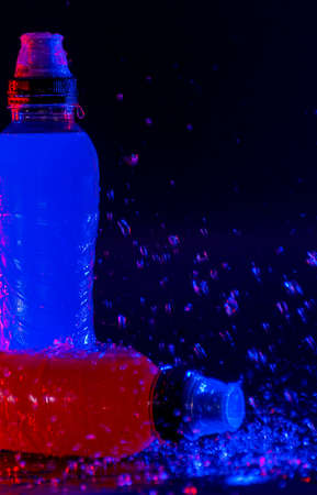 Isotonic drinks for sportsmen, on background black and punctuated by jets of waterの写真素材