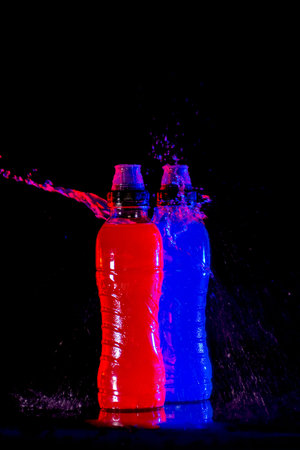 Isotonic drinks for sportsmen, on background black and punctuated by jets of waterの写真素材