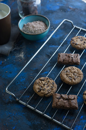 fresh homemade chocolate cookies on a baking tray accompanied by a cup of milk