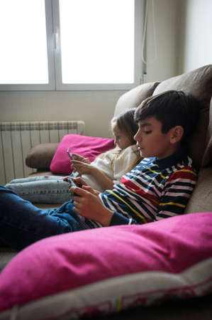 Children happily playing video games on the home sofaの写真素材