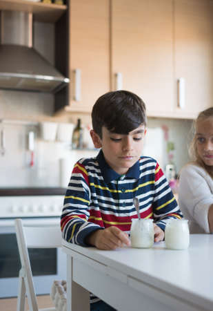 Happy children eating a yogurt in the dining room of their houseの写真素材