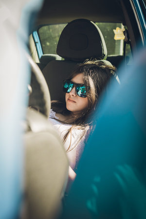 Teen girl sitting in the car looking at her smartphone on a summer afternoon