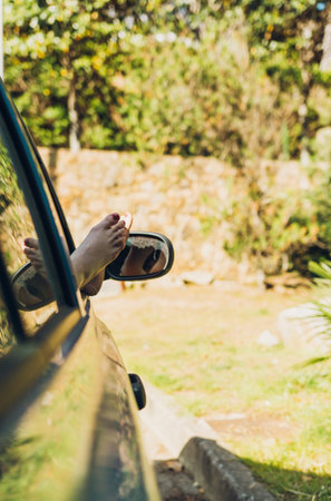 Girl with her feet out of the window of the car sunbathing on a summer afternoon, while traveling...