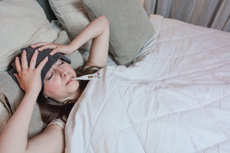 Sick teenage girl with a high fever and a thermometer. She has a cold.