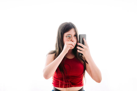 Teenage girl putting on a little makeup, seeing herself reflected on the screen of her mobile phone.