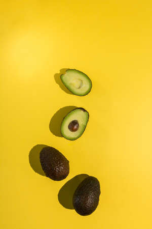 Avocados cut on a background of color and reflected shadows of palm leafの写真素材