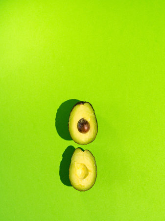 Fresh avocado on a green background accompanied by leaves and shadows of the plants.