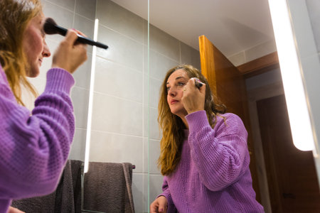 40-year-old woman putting on makeup and taking care of her skin in the bathroom before going to workの写真素材