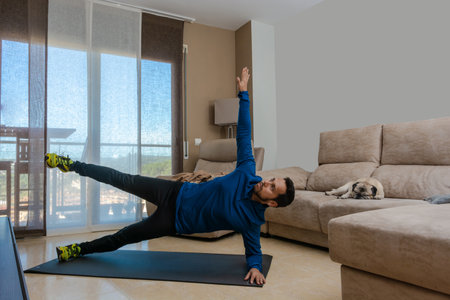 Latin man, doing a workout in his living room, does sit-ups, stretches and squatsの写真素材